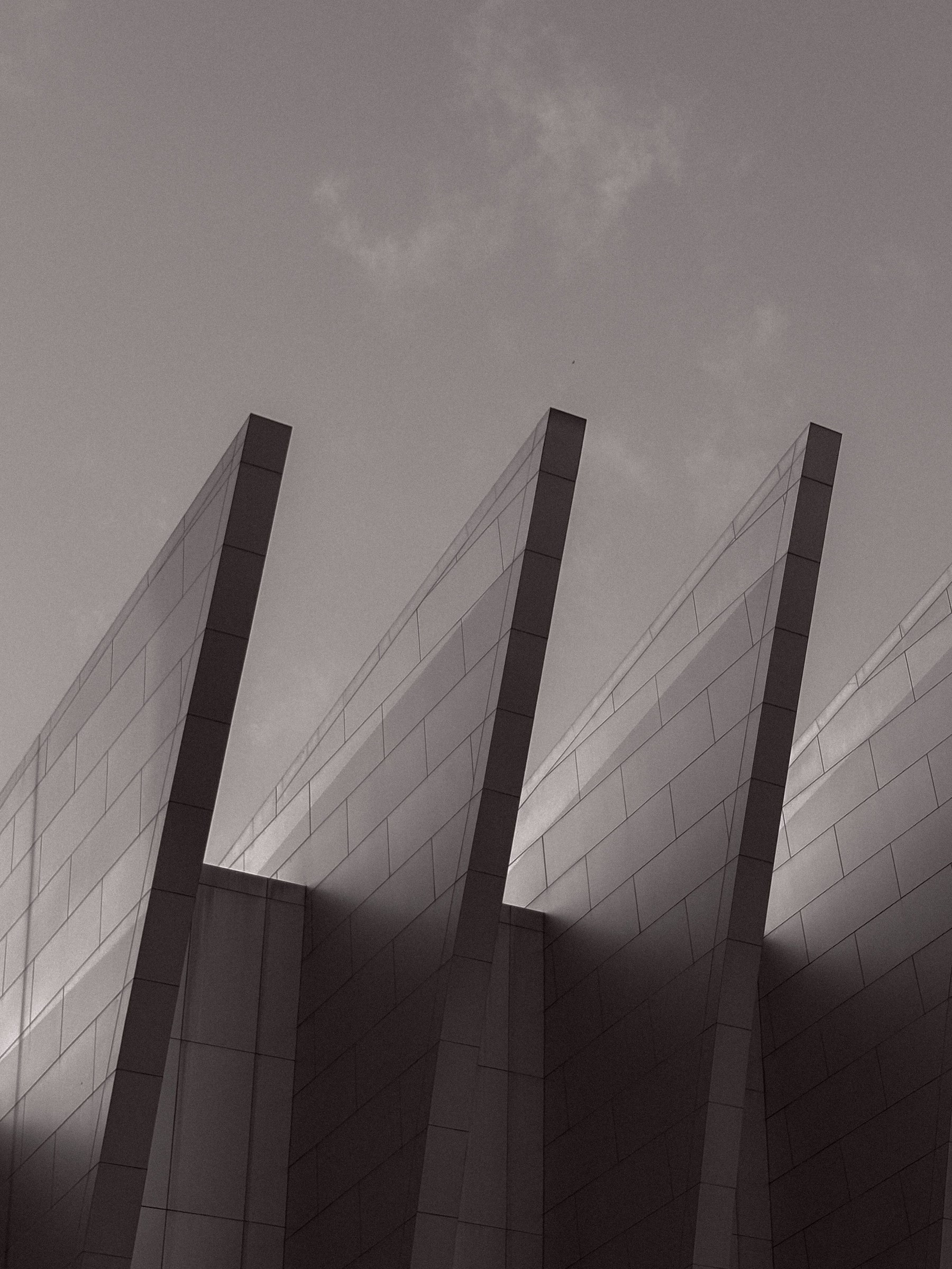 Black-and-white photograph of angular steel facades rising against a cloudy sky.